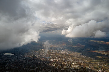 Aerial view from airplane window at high altitude of distant city covered with puffy cumulus clouds...