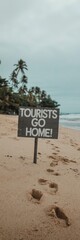 "Beach Scene with 'Tourists Go Home!' Sign, Footprints, Palm Trees, and Overcast Sky"