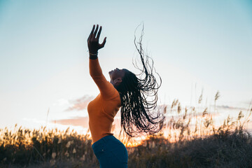 Young woman dancing with flowing hair at sunset in a field