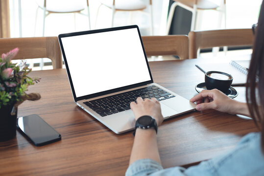 Mockup blank white screen laptop computer. Business woman using and searching the information on laptop with empty screen on wooden table in modern loft cafe. 