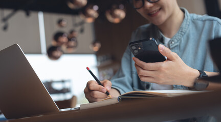 Woman using mobile phone and working on laptop computer at coffee shop. Happy asian woman online working, surfing the internet using smartphone and laptop, freelance at work