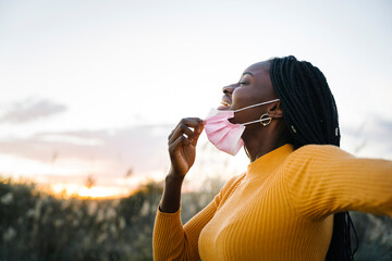 Happy woman taking off a surgical mask and breathing deeply in a field at sunset
