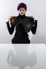 A stylish Muslim woman in a hijab presents her innovative handmade fashion accessory crafted from...