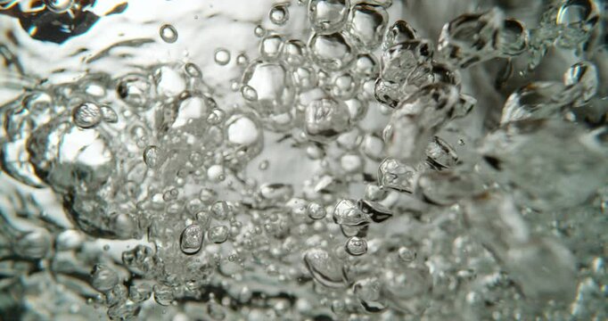 Extreme close-up view of hot water boiling in saucepan. The water creates mesmerizing forms and shapes. Static slow-motion shot