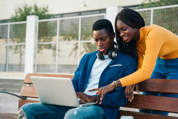 Two young black professionals working on laptop outdoors