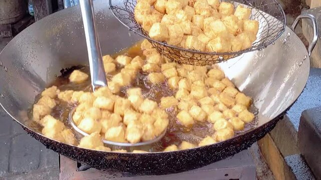 Cinematic shot. The cooking process of Tofu being deep-fried, likely for a dish called Crispy Pong Tofu, a popular Indonesian street food