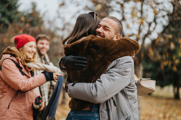 Happy friends meet in a park during a crisp autumn day, sharing hugs and smiles, surrounded by...