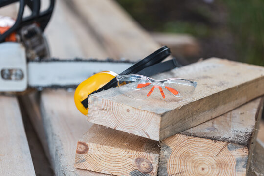 A pair of safety glasses and a chainsaw are on a wooden surface
