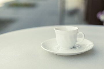 A white coffee cup sits on a white plate on a table