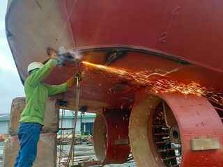 A shipyard technician uses a gas welding torch to cut and repair the bottom part of a ship. A heavy...