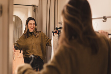 Modern young woman has opportunity to evaluate how she is wearing in fitting room of clothing store. Fashionable clothes. Shopping and pleasure. Happy smiling wow woman make choice of two jeans.