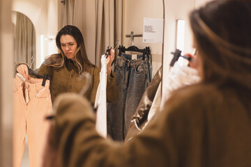 Modern young woman has opportunity to evaluate how she is wearing in fitting room of clothing store. Fashionable clothes. Shopping and pleasure. Sad woman not like clothes jeans in mall, look unhappy.