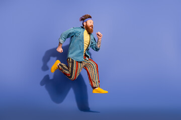Stylish man with red hair and vibrant retro outfit jumps against a vivid purple background, capturing energy, humor