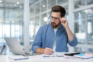 Serious thinking financier accountant working with computer inside office. Man doing paperwork,...