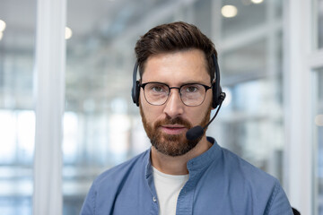 Webcam view, man with headset looking into camera, support worker talking to customers. Male...