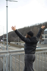 Person celebrating on a bridge over highway with raised arms overlooking traffic below during an...
