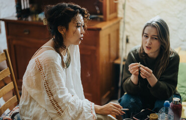 Two friends are seated indoors, sharing a moment while engaged in conversation and smoking. The...