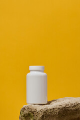 White plastic medicine jar on stone, yellow background. Mock up