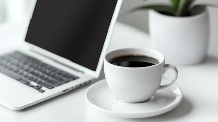 Coffee cup beside a laptop and plant.