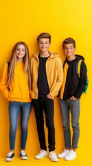 Obraz premium Three teenagers, a girl and two boys, stand together against a vibrant yellow background, showcasing their youthful energy and style.