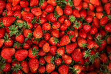 Fresh ripe strawberries with green leaves, piled together in a market setting. Vibrant red color and juicy texture, perfect for food, health, and organic produce concepts.