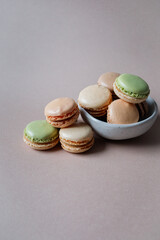 French multicolored mini macarons in a small bowl on beige background