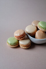French multicolored mini macarons in a small bowl on beige background close up