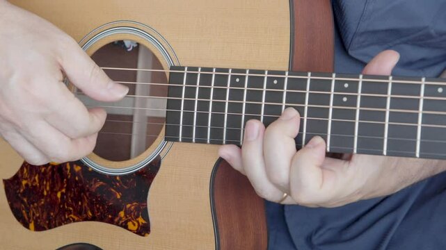 Persona tocando una guitarra ac&uacute;stica. Se ven solo sus manos y pareciera estar recibiendo lecciones o estudiando el instrumento.