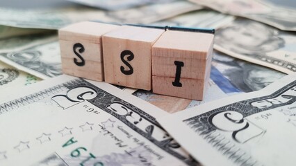 SSI acronym made of wooden letter cubes on pile of US dollar banknotes. Supplemental Security Income