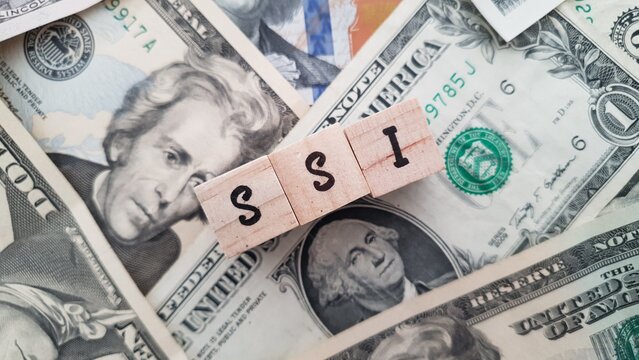 SSI acronym made of wooden letter cubes on pile of US dollar banknotes. Supplemental Security Income