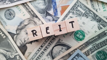 REIT acronym made of wooden letter cubes on pile of US dollar banknotes. Real Estate Investment Trust