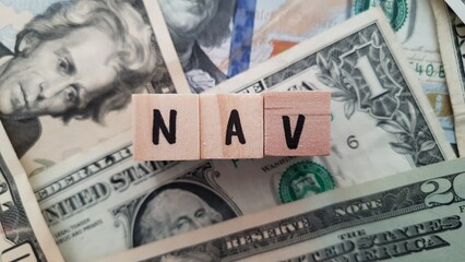 NAV acronym made of wooden letter cubes on pile of US dollar banknotes. Net Asset Value © xsprtd