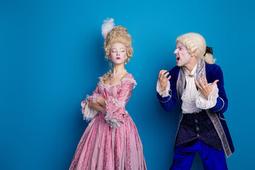 Elegantly dressed couple arguing in vintage baroque costumes, set against a striking blue background
