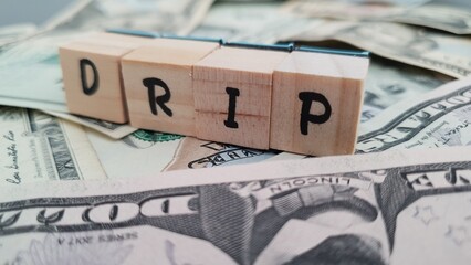 DRIP acronym made of wooden letter cubes on pile of US dollar banknotes. Dividend Reinvestment Plan © xsprtd