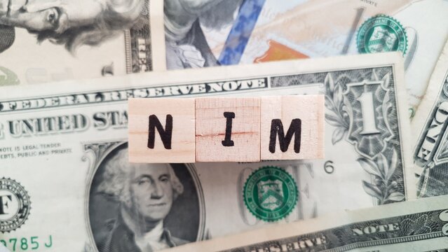 NIM acronym made of wooden letter cubes on pile of US dollar banknotes. Net Interest Margin