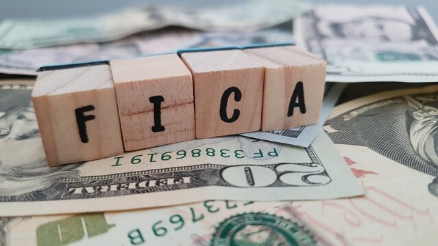 FICA acronym made of wooden letter cubes on pile of US dollar banknotes. Federal Insurance Contributions Act