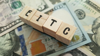 EITC acronym made of wooden letter cubes on pile of US dollar banknotes. Earned Income Tax Credit