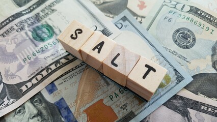 SALT acronym made of wooden letter cubes on pile of US dollar banknotes. State and Local Tax