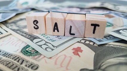 Obraz premium SALT acronym made of wooden letter cubes on pile of US dollar banknotes. State and Local Tax