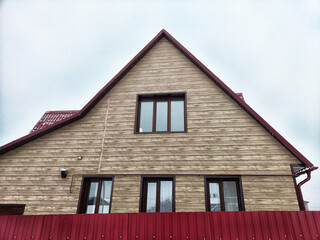 Modern wooden house with red roof and fence in a quiet suburban area during an overcast day