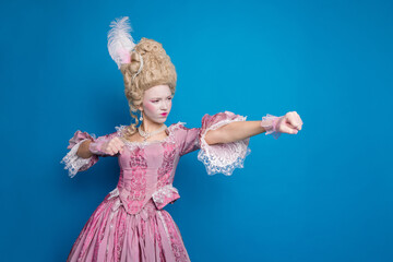 Elegant young woman poses in an elaborate pink baroque costume against a vibrant blue background