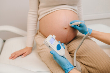 Gynecologist listens to fetus heartbeat with fetal doppler in the clinic. Gynecologist checks heart...