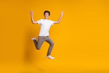 Happy young man with curly hair jumping in casual attire on a yellow background, expressing joy and energy for lifestyle