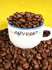 Closeup of fresh whole brown coffee beans in and around an overflowing espresso cup.
