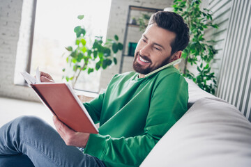 Handsome man multitasking while talking on phone and reading book in modern cozy living space