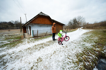 Winter adventure unfolds as a child plays with a pink bicycle near a cozy rural house surrounded by...