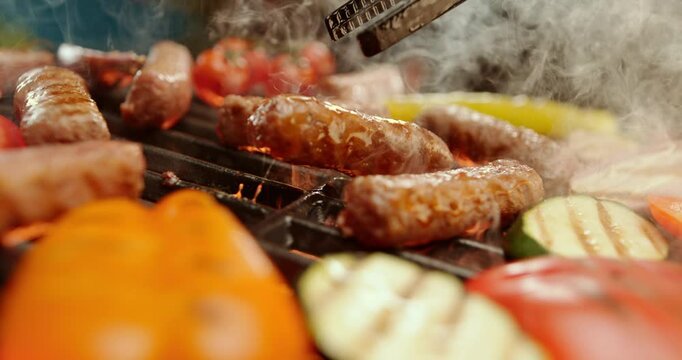 Slow-motion footage of a professional chef placing freshly prepared ćevapčići (Balkan-style minced meat sausages) onto a hot grill with tongs. Smoke and sizzling juices rise as the meat sears over glo