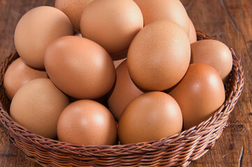 Raw brown eggs arranged in a basket with a rustic wooden background