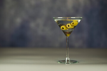 Refreshing Martini glass with green olives inside, on a grey surface