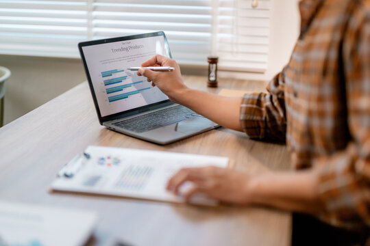 Businesswoman pointing at laptop screen showing trending product data while analyzing paperwork